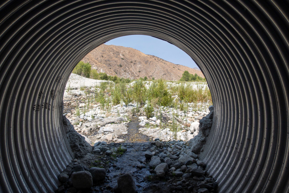 View from inside a corrugated culvert pipe looking out onto the riverbed.